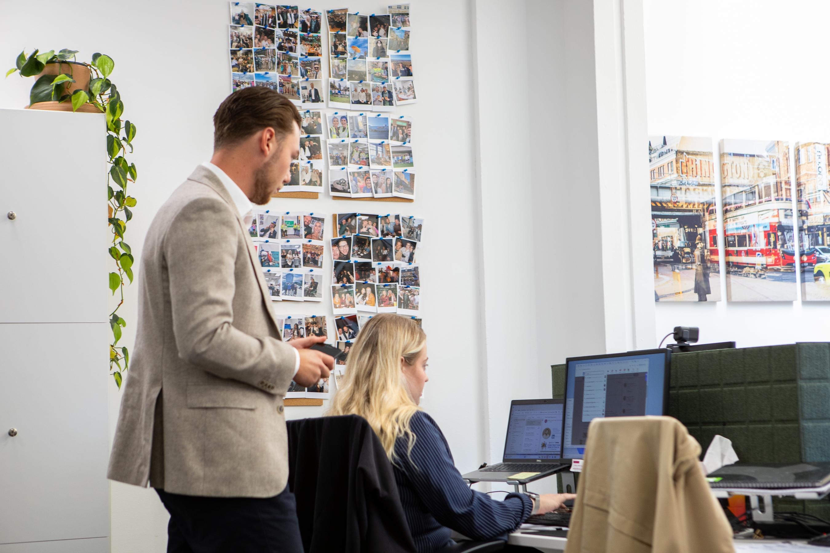 Coworkers collaborating in a modern office with laptops and photo wall
