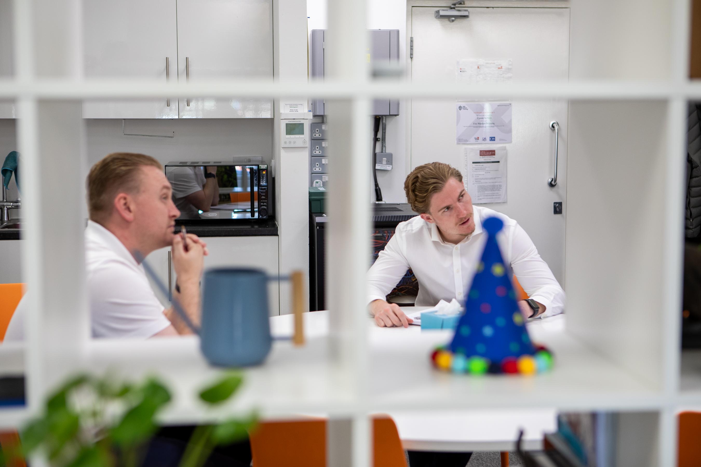 Two men in an office break room having a discussion at a table